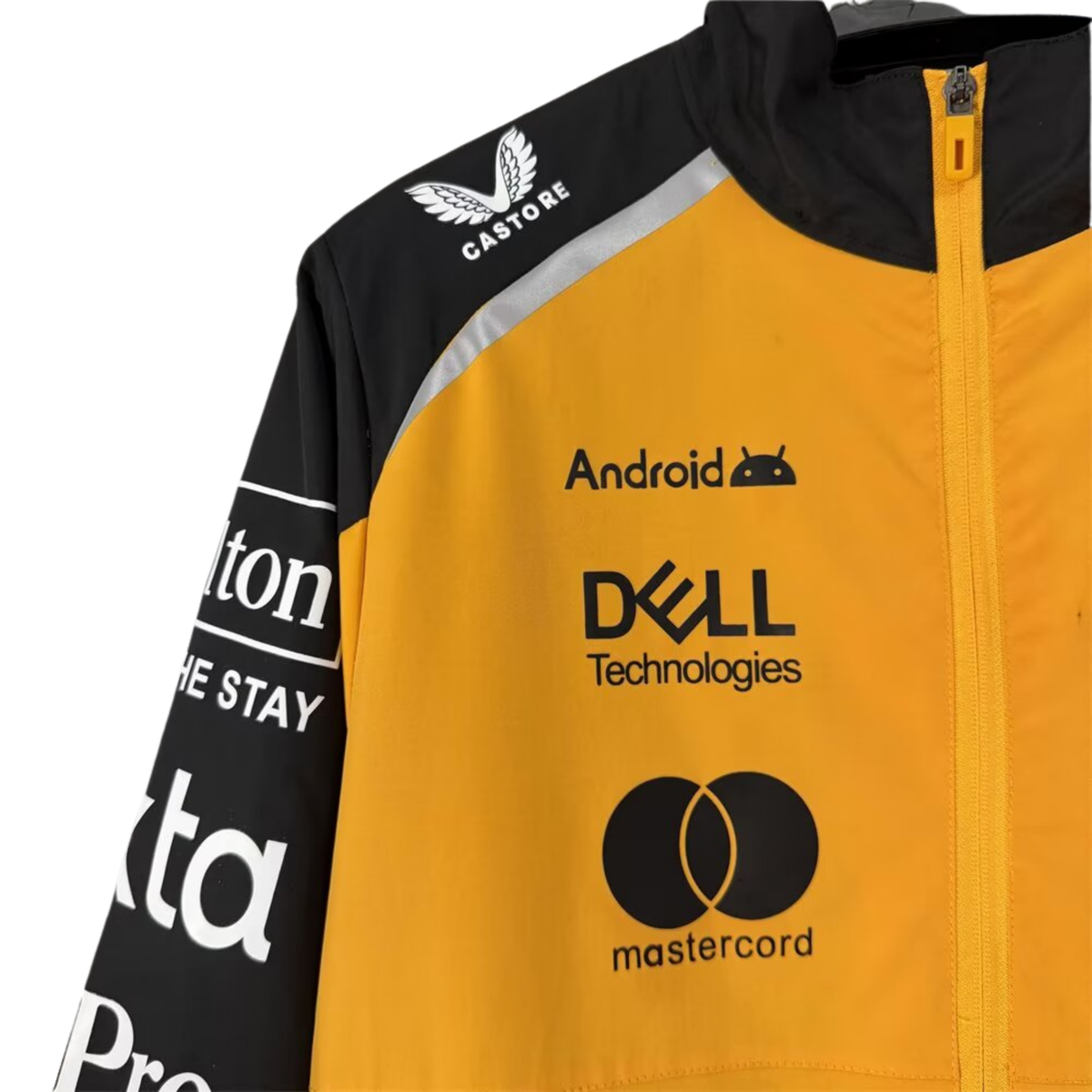 A papaya orange and black McLaren F1 2026 team windbreaker jacket featuring a full front zipper, stand-up collar, and sponsor logos including Android, Dell Technologies, and OKX across the chest.