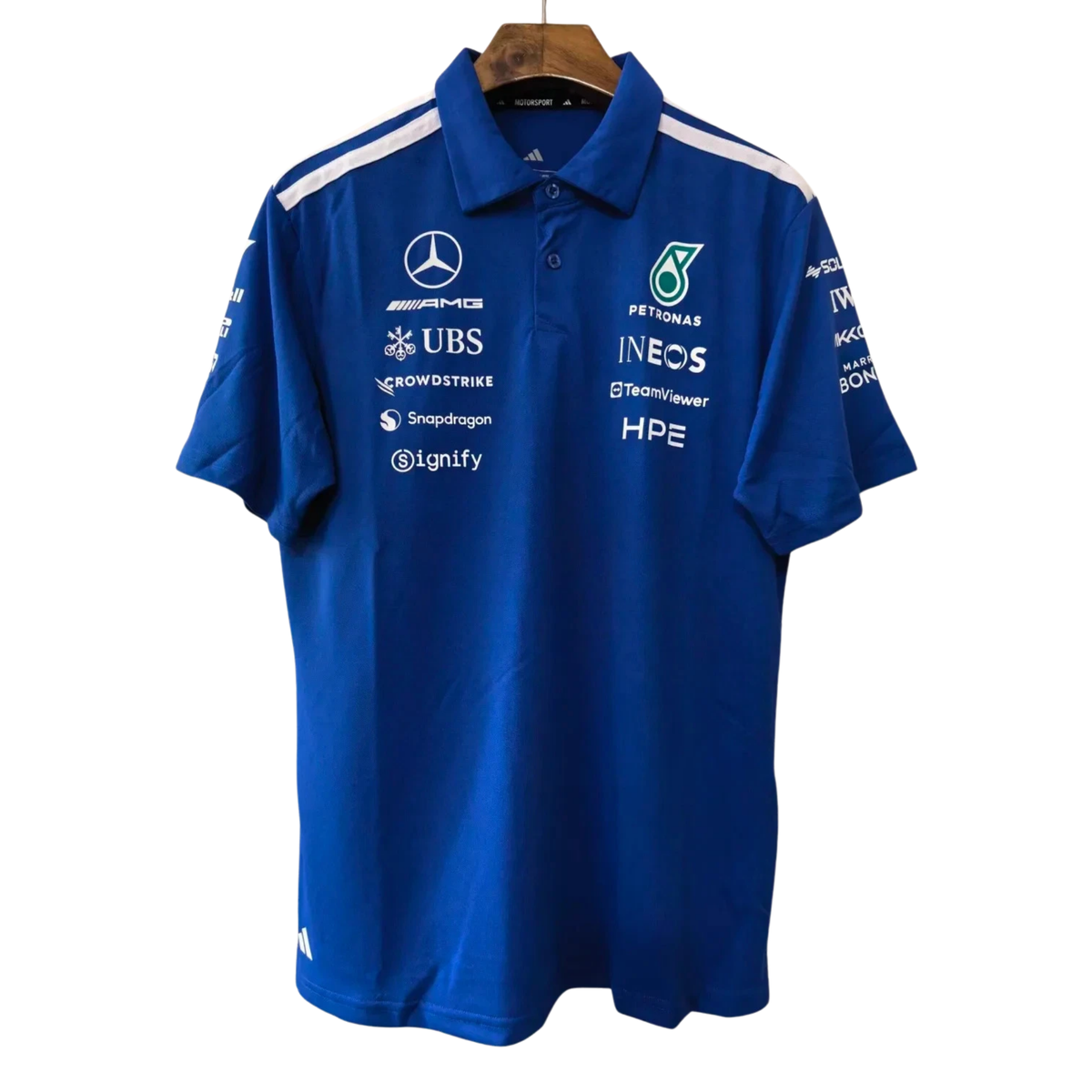 A royal blue Mercedes-AMG Petronas 2026 team polo shirt featuring a classic collar with white shoulder stripes, a button placket, and official partner logos including Mercedes-AMG, Petronas, and UBS across the chest.