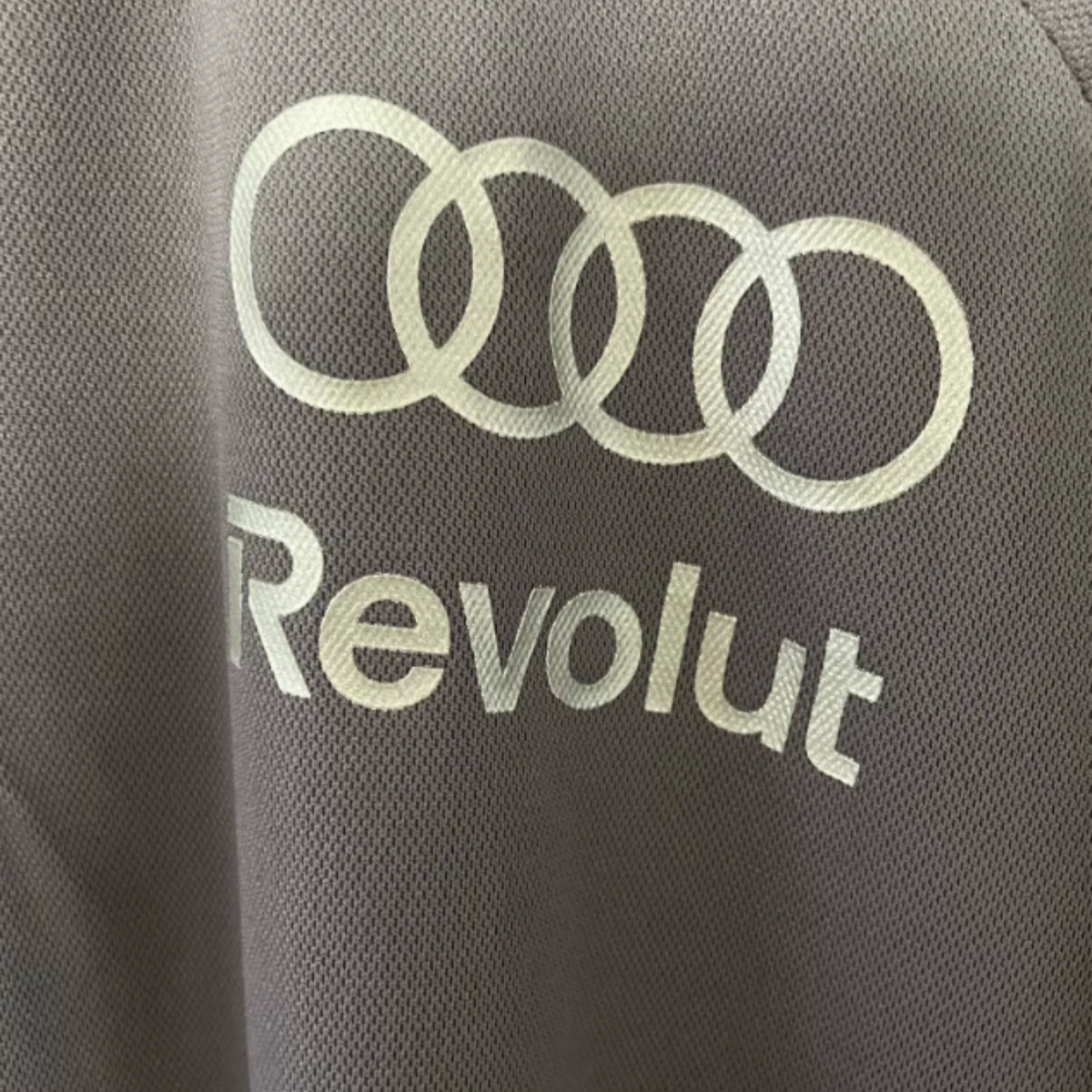 Official Audi 2026 team polo shirt in dark grey, featuring sponsor logos including Revolut, adidas, and Castrol.