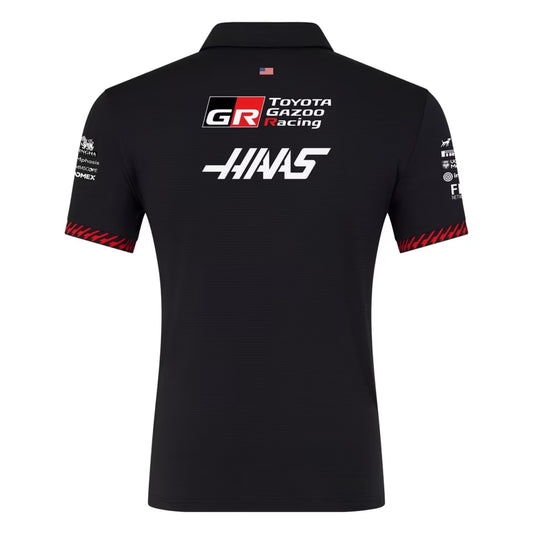 A black and red MoneyGram Haas F1 Team 2026 team polo shirt featuring a classic collar with a short zipper placket, red shoulder accents, and official partner logos including MoneyGram Haas F1 Team, Toyota Gazoo Racing, and Orion180 across the chest.