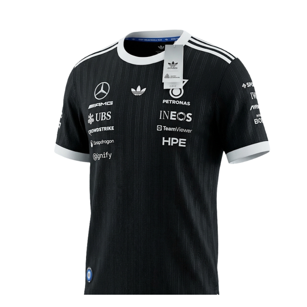 A black and white Mercedes-AMG Petronas 2026 black edition t-shirt featuring an all-over vertical pinstripe pattern, a white crew neck and sleeve cuffs with white shoulder stripes, and official partner logos including Mercedes-AMG, Petronas, and UBS across the chest.