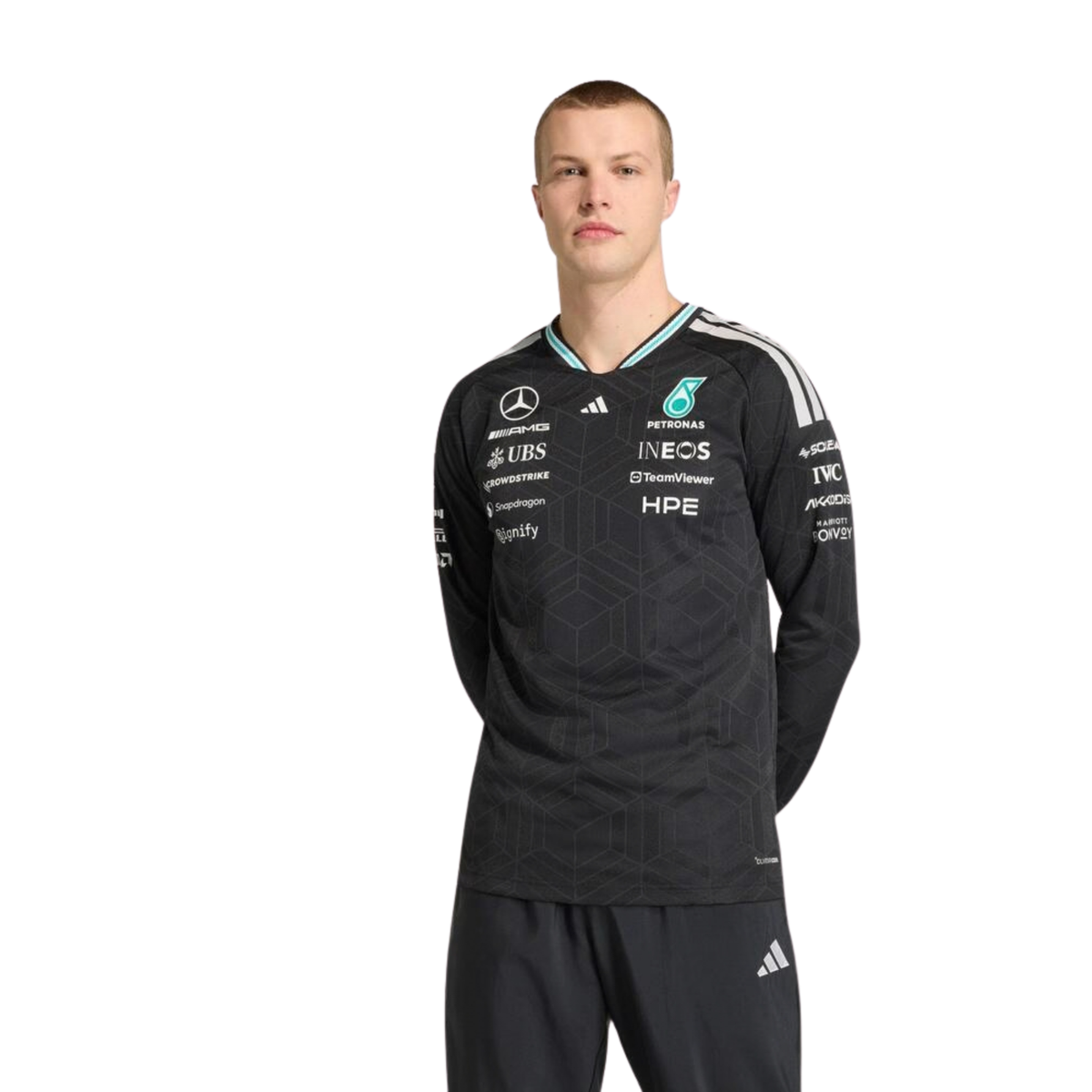 A black Mercedes-AMG Petronas 2026 team long-sleeve t-shirt featuring an all-over tonal geometric pattern, a V-neck collar with white shoulder stripes and vibrant teal inner trim, and official partner logos including Mercedes-AMG, Petronas, and UBS across the chest.