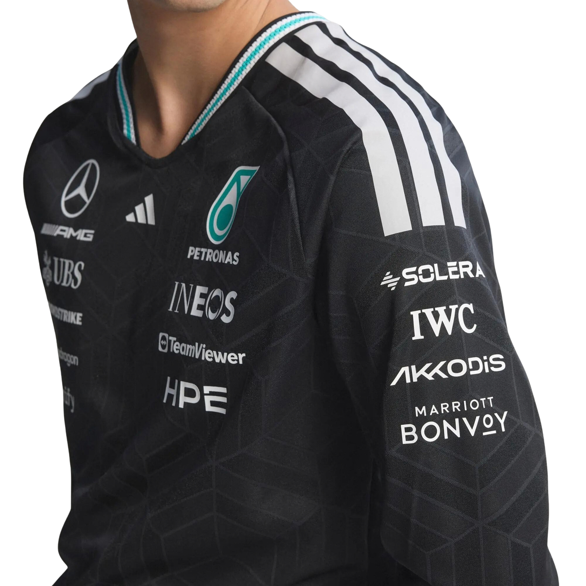 A black Mercedes-AMG Petronas 2026 team long-sleeve t-shirt featuring an all-over tonal geometric pattern, a V-neck collar with white shoulder stripes and vibrant teal inner trim, and official partner logos including Mercedes-AMG, Petronas, and UBS across the chest.