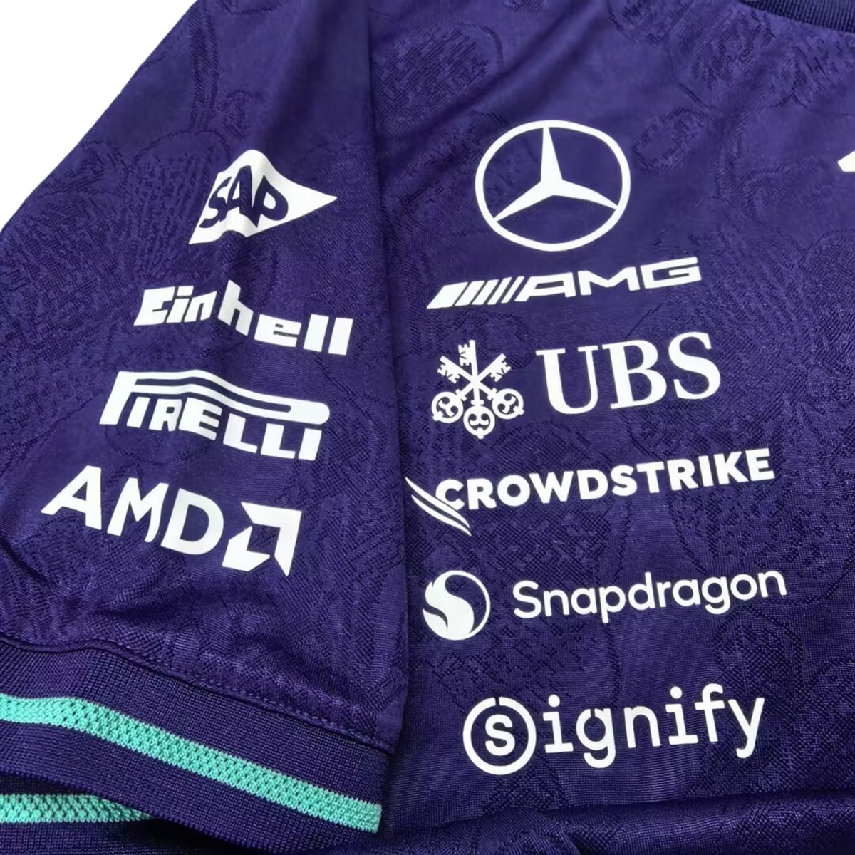 A special edition purple and teal Mercedes-AMG Petronas 2026 Singapore GP team t-shirt featuring an all-over tonal floral pattern, a crew neck with teal trim, and official partner logos including Mercedes-AMG, Petronas, and INEOS across the chest.