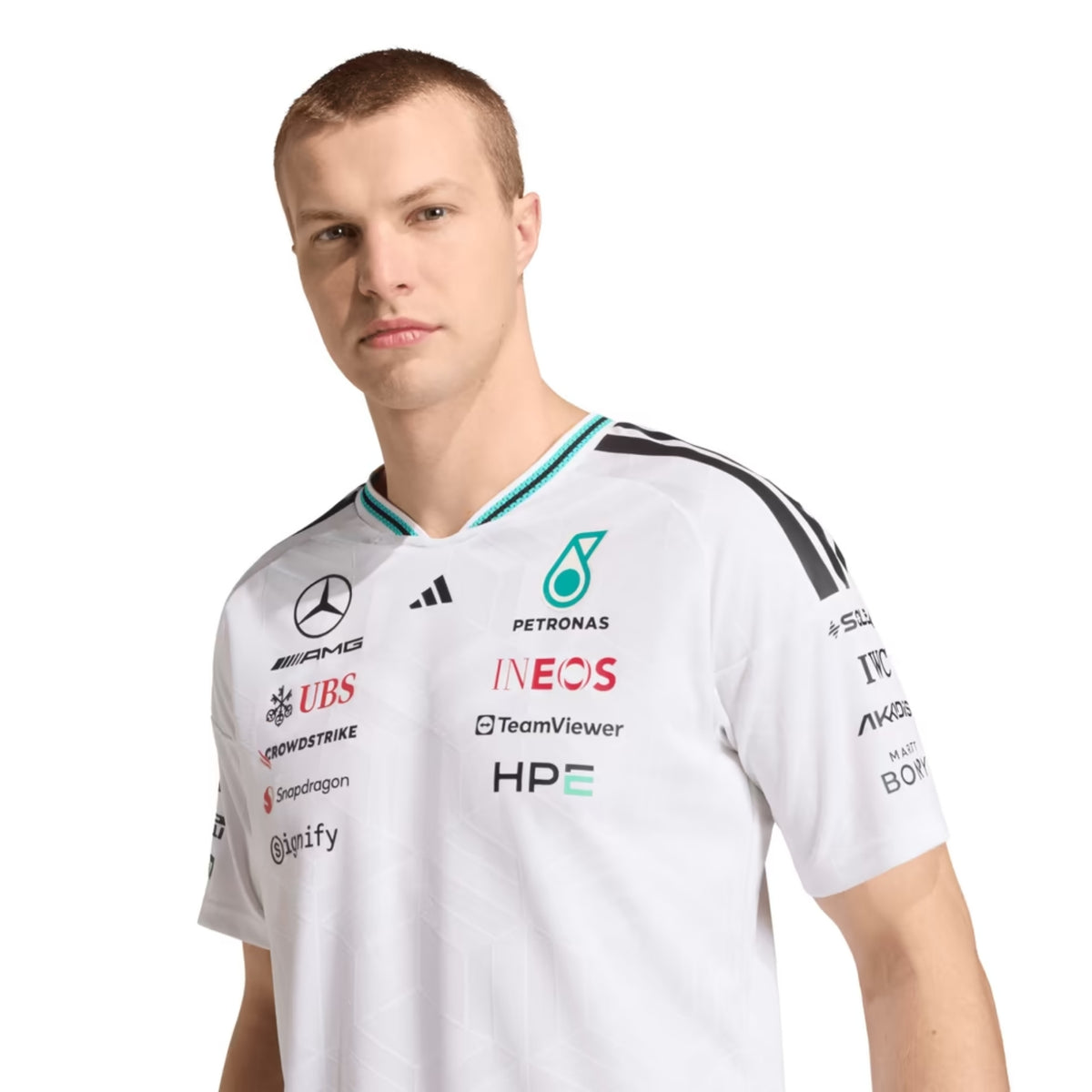 A white Mercedes-AMG Petronas 2026 team t-shirt featuring a V-neck with black shoulder stripes, teal inner collar detailing, and official partner logos including Mercedes-AMG, Petronas, and INEOS across the chest.