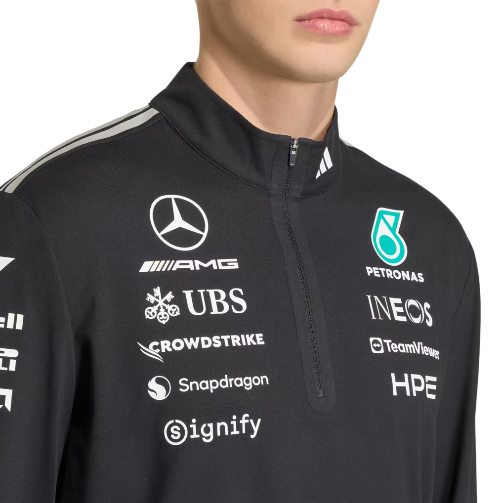 Model wearing a black Mercedes-AMG Petronas F1 2026 team 1/4-zip sweatshirt with sponsor logos including Adidas, UBS, and CrowdStrike
