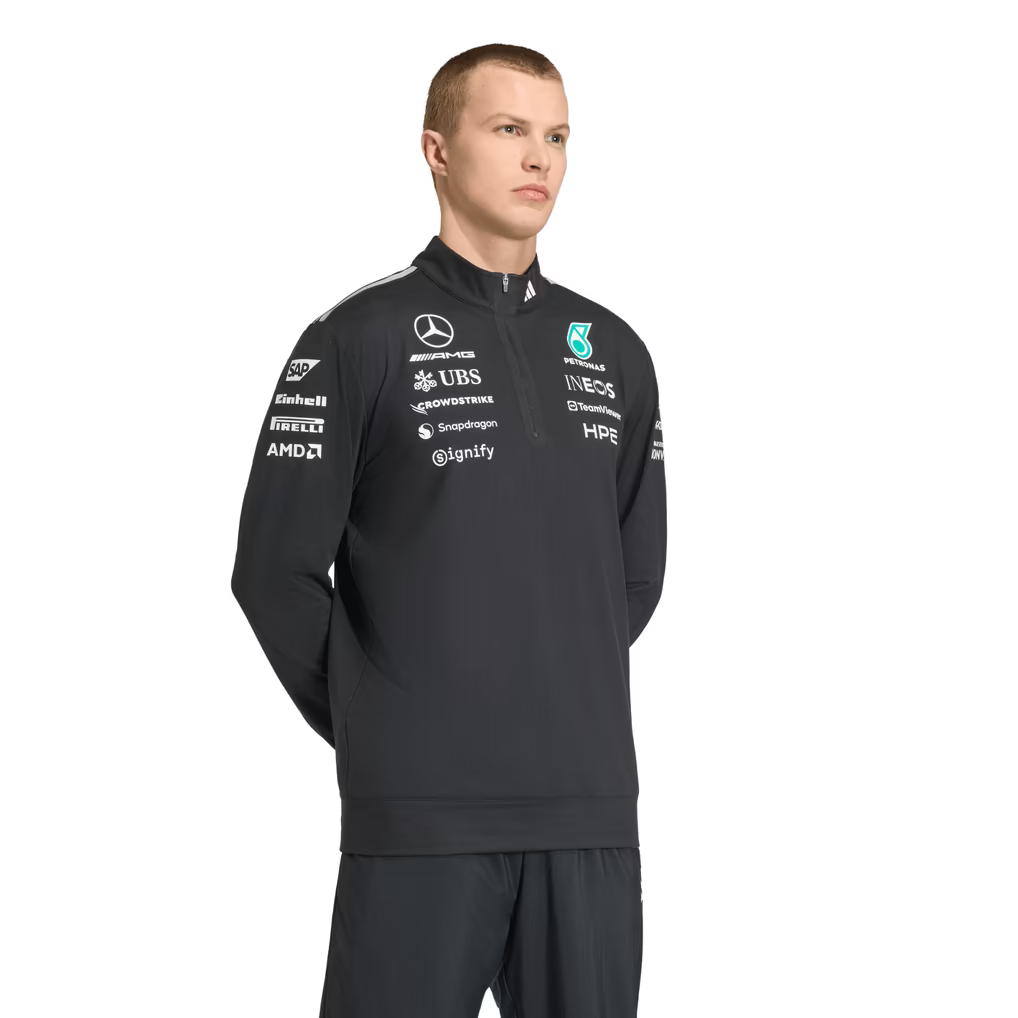 Model wearing a black Mercedes-AMG Petronas F1 2026 team 1/4-zip sweatshirt with sponsor logos including Adidas, UBS, and CrowdStrike