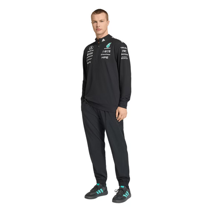 Model wearing a black Mercedes-AMG Petronas F1 2026 team 1/4-zip sweatshirt with sponsor logos including Adidas, UBS, and CrowdStrike