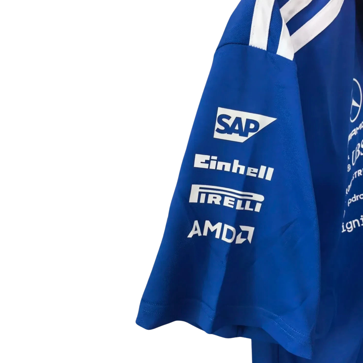 A royal blue Mercedes-AMG Petronas 2026 team polo shirt featuring a classic collar with white shoulder stripes, a button placket, and official partner logos including Mercedes-AMG, Petronas, and UBS across the chest.