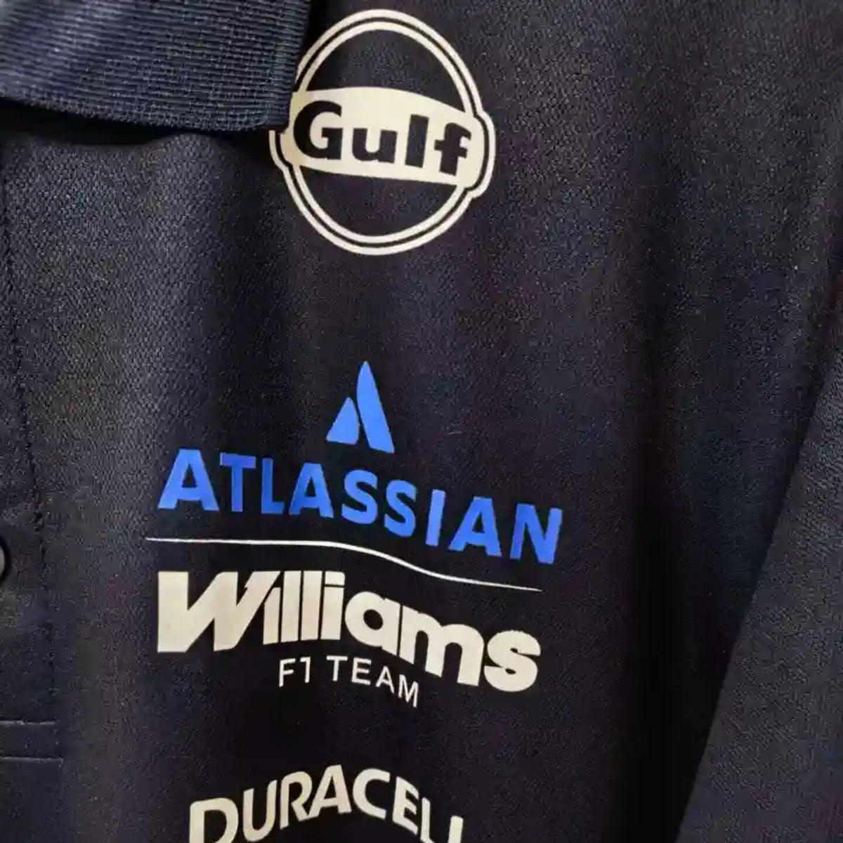 Official Williams Racing 2026 team polo shirt in navy blue, featuring sponsor logos including Gulf, Komatsu, and Duracell.