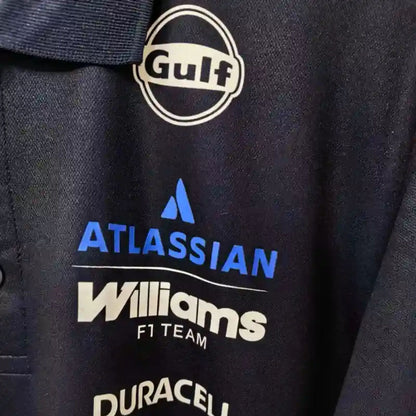 Official Williams Racing 2026 team polo shirt in navy blue, featuring sponsor logos including Gulf, Komatsu, and Duracell.